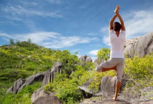 fitness, sport, people and recreation concept - young man making yoga tree pose on beach from back over natural background